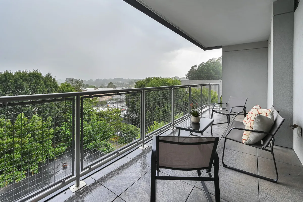 This exterior image shows a balcony area with outdoor seating, a potted plant, and an expansive view of the surrounding landscape. The scene feels welcoming and immediately accessible, suggesting ease of arrival and relaxation after a journey. The clean, well-maintained look of the balcony hints at attentive management and the promise of a trouble-free stay.