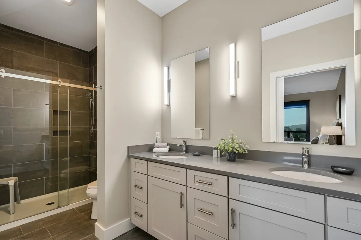 A sophisticated ensuite bathroom equipped with a double vanity, expansive mirrors, and a modern glass shower enclosure. The design is both functional and relaxing, perfect for unwinding after a day out.