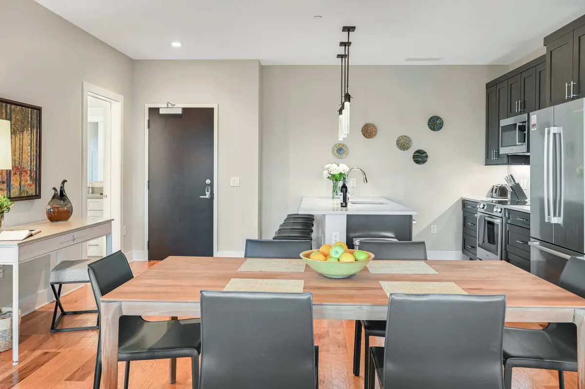 An inviting dining area with a fruit bowl centerpiece, a spacious kitchen counter and black cabinetry, accented by decorative wall art. The space feels perfect for gathering with friends or family after a day of seasonal activities downtown or in nature.