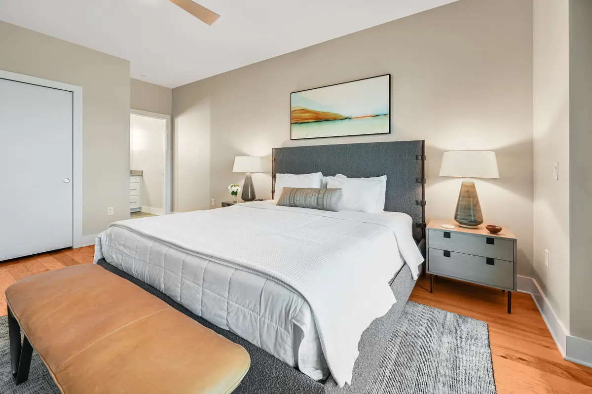 A stylish king bedroom with elegant bedding, a cozy bench at the foot of the bed, and tasteful artwork. Natural light streams in, enhancing the room’s inviting and calming quality.