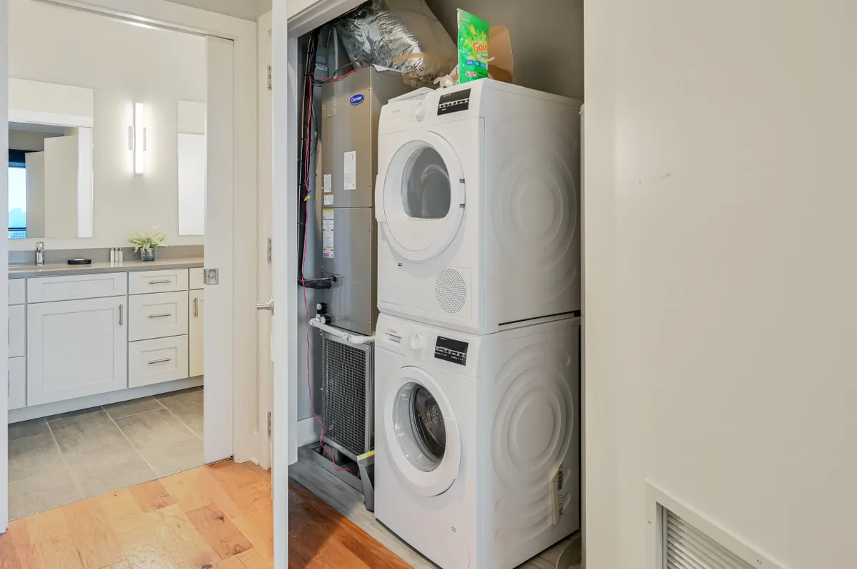 This image presents a modern laundry area with stacked washer and dryer, sleek cabinetry, and a mirror. The space is clean, efficient, and practical, reflecting the behind-the-scenes care and convenience offered by 24/7 local management. It subtly reinforces the idea that all guest needs—from check-in to everyday living—are thoughtfully addressed.