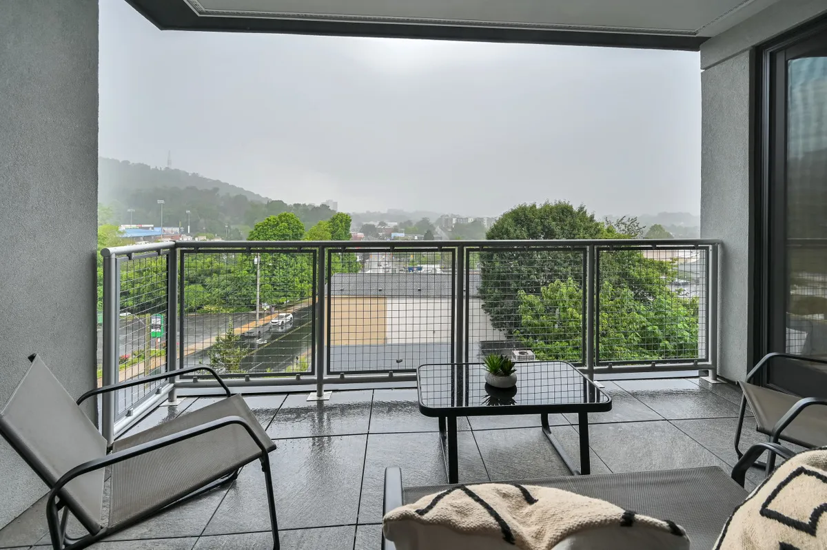 A serene balcony scene overlooking the city, featuring inviting seating and a potted plant. The vantage point suggests a cozy space for couples to relax and soak in the urban atmosphere, with easy access to downtown just below.