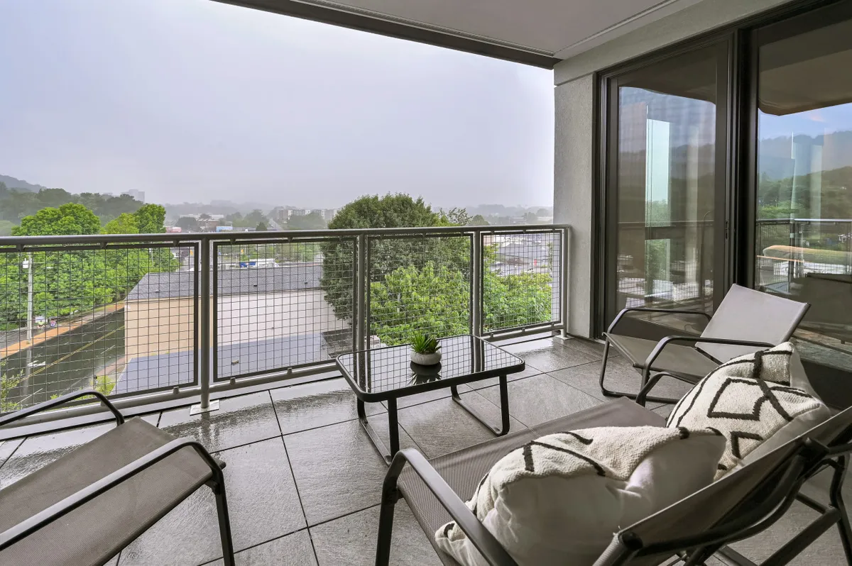 An exterior balcony with comfortable seating, overlooking green tree-covered hills. The view is peaceful and lush, with natural elements that echo the region's scenic mountain beauty.