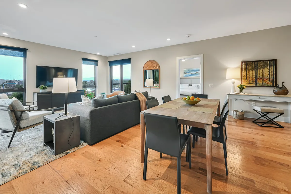 A stylish and cozy open living space with a modern dining table, plush seating area, and expansive windows that flood the room with light. Thoughtful décor and artwork lend warmth, while the layout seamlessly connects the dining and living zones for socializing or quiet moments.