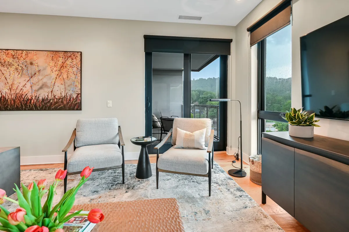 A tranquil living area featuring comfortable chairs arranged around a coffee table, with tasteful artwork on the wall and a television in view. Gentle morning light streams through the windows, creating an inviting space perfect for relaxing or informal meetings.