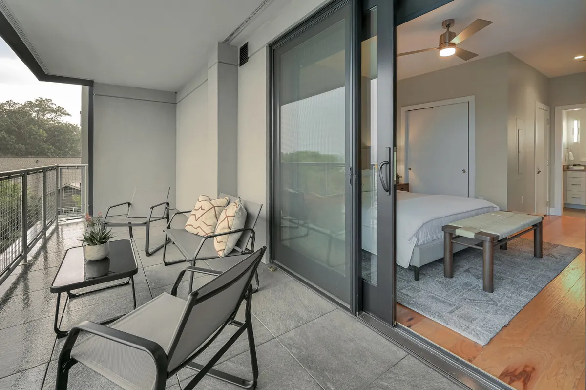 This image shows a stylish balcony seating area with comfortable chairs overlooking the outdoors. The open sliding door connects the interior suite to the private balcony, inviting guests to step out and take in expansive views. Warm sunset light bathes the scene, emphasizing the sense of relaxation and exclusivity.